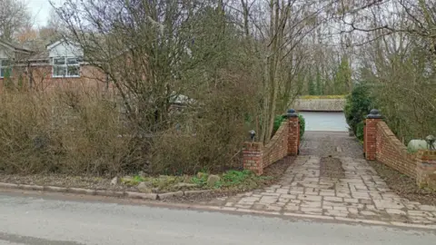 A view from the road of the light green garage door behind a driveway where Spiby hid his luxury cars and drug lab