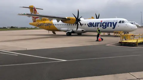 BBC A yellow and white plane with the word Aurigny on the side of the fuselage. 