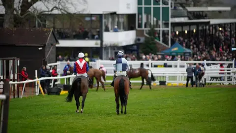 Getty Images Two jockeys riding horses on a race track with their backs to the camera. There is a crowd in front of them.