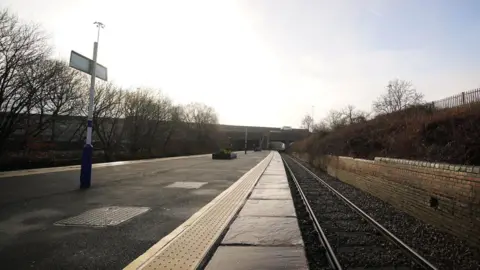 A deserted Denton railway station in Tameside, Greater Manchester, has two platforms. It is photographed on a grey winter's day.