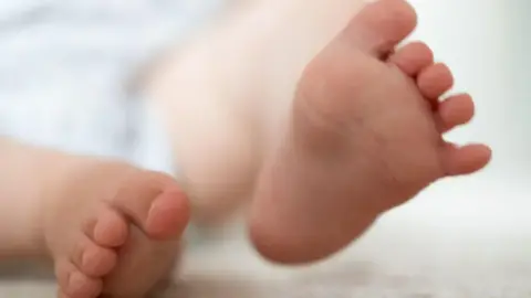 A stock image of a pair of baby feet. The child is lying on a blanket, with its lower legs, feet and toes showing in the centre of the image. 