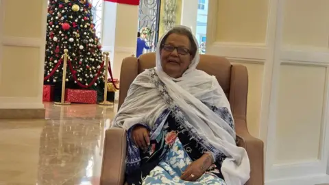 Tutu Melaku Tutu's mother Asnakech is sitting on a chair and behind a big Christmas Tree.
