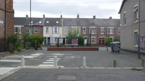Newcastle City Council The space before the garden was built, which was an empty space of grey concrete slabs. The house which now features the mural was similarly grey, as was the sky.