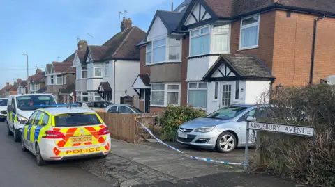 Tony Fisher/BBC A Google Streetview look at Kingsbury Avenue. Blow's Downs are on the horizon and there's semi-detached houses on either side of the road which runs down the middle of the shot. Cars are parked half on the road and pavement