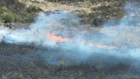 DFRS Derbyshire Fire and Rescue Service damping down flames at a wildfire off Woodhead Pass at Woodhead Reservoir, near Glossop, Derbyshire.