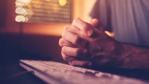 Getty Images Man with hands clasped at keyboard