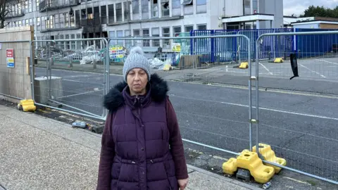 Irina Vasile in a purple coat standing in front of Spectrum House, which has been fenced off.