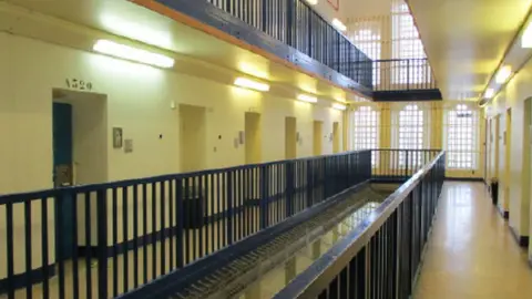 The inside of a prison with cream walls and black metal bars.