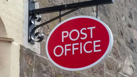 A red oval Post Office sign attached to a brick wall.