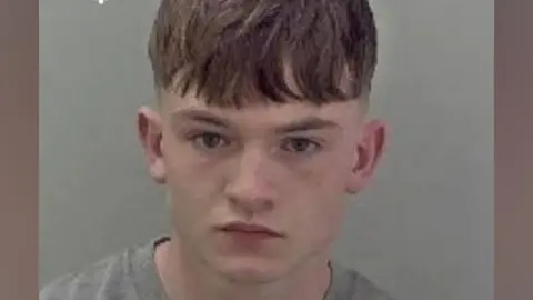 A mugshot of Alex Quinn, who is a young-looking man with short brown hair wearing a grey T-shirt.