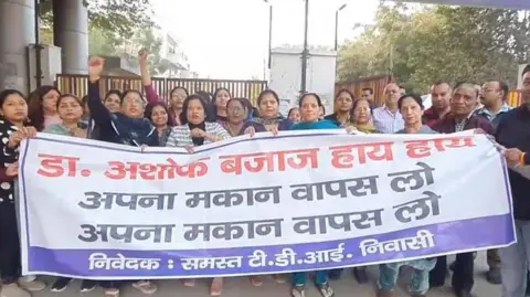 Protesting residents of AK Mishra were seen holding a banner calling on Dr Ashok Bajaj to take back the sale of his house.