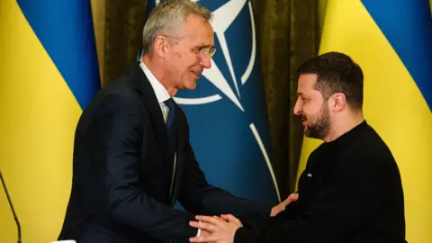 Getty Former Nato secretary-general Jens Stoltenberg smiles as he shakes hands with the Ukrainian President Volodymyr Zelensky in front of Nato and Ukrainian flags at a meeting in Kyiv in May 2023.