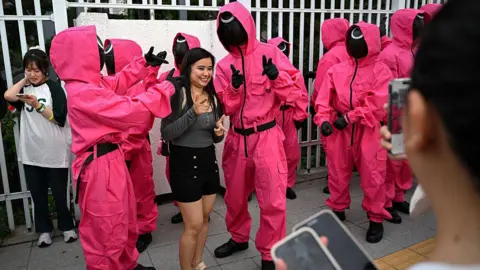 Getty Images Pink Guards of Squid Game pose for a photograph with a fan during a parade event