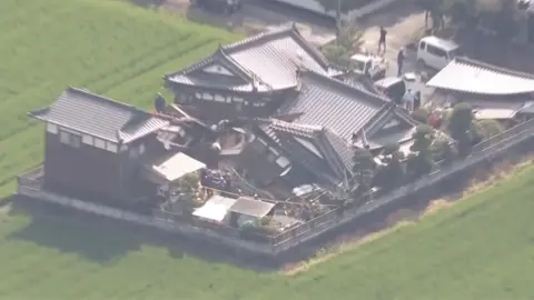 A damaged building is seen surrounded by green grass.