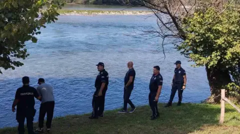 Six men, five of which in police uniform, standing on a bank of a river