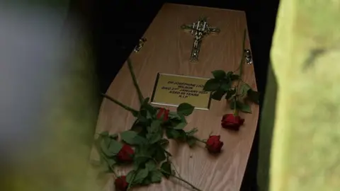 Close up of the plate on Jo's coffin giving details of her, with roses thrown on top