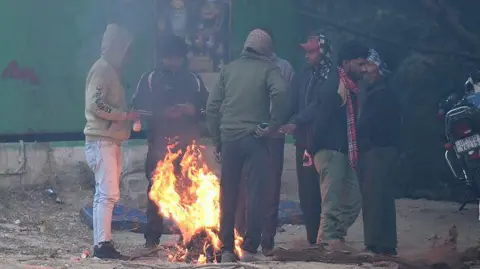 Getty Images Seven men are standing around bonfires, wearing sweaters and jackets to protect themselves from the cold.