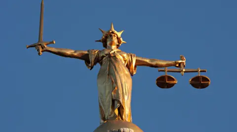 BBC A figure of Lady Justice in gold, seen against a blue sky.