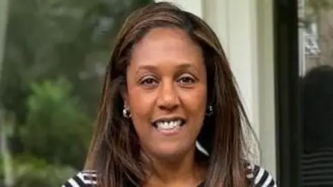 Nancy Smith Nancy Smith with long, dark brown hair smiling at the camera and wearing a blue and white striped T-shirt. She is standing by a wooden door with a glass window, and in front of a garden.