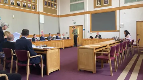 The council chamber showing chairs and desks with smartly dressed people seated around the room