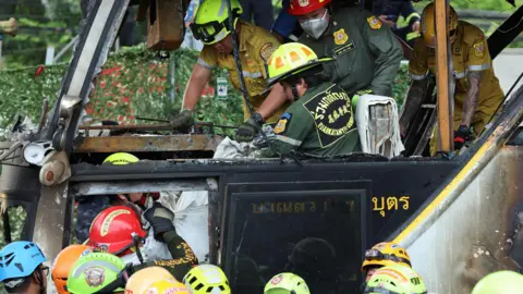 Reuters Firefighters transfer bodies from a burnt-out bus that was carrying teachers and students from Wat Khao Phraya school, 