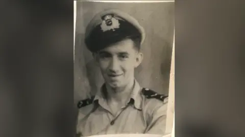Family picture An old black and white photograph. It has a man that is clean shaven and has a naval hat on. He is dressed in uniform.