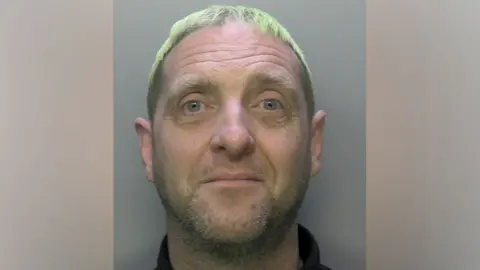 Surrey Police A mugshot of a man with short white hair.