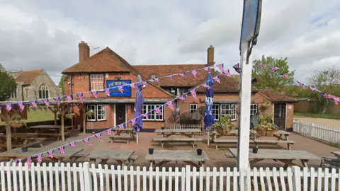 A red brick pub with benches and Union Flag bunting in the front garden.