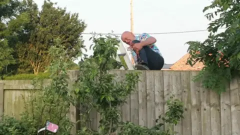 Cllr Matthews climbing over the fence