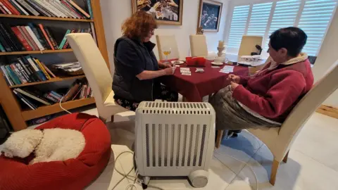 BBC News Two women play cards by an electric heater