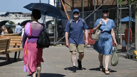 Getty Images People wearing caps or holding an umbrella walk in the heat in London