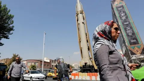 AFP A woman walks past a Shahab-3 ballistic missile and launcher on a street in Tehran, Iran, during Defence Week (26 September 2019)