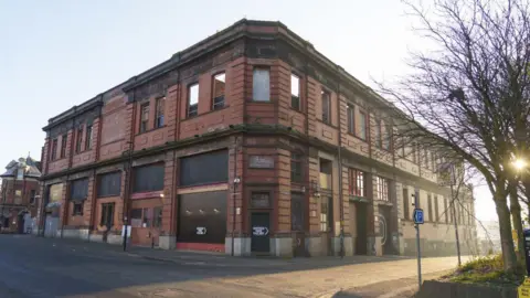 Getty Images is an old building of Victorian red brick that is displayed from the corner, with empty roads that feed on the left and right. The building appears abandoned with some windows and doors ascending.