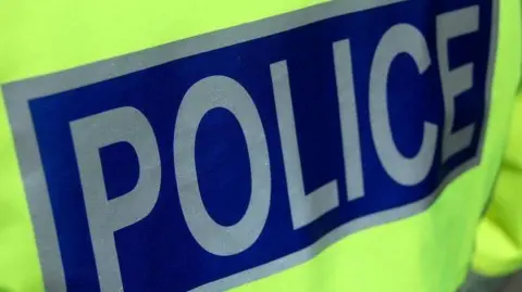 A close up of a police officer's high visibility jacket. The word police is in silver letters on a dark blue background.