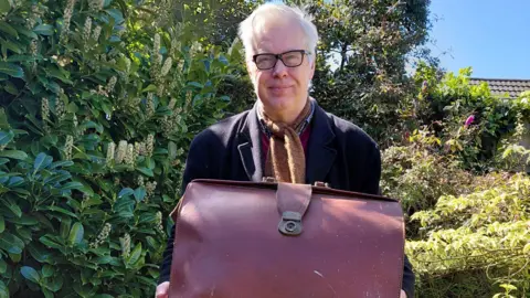 Mark Wilson Mark Wilson standing in his garden, holding an old, brown, leather briefcase