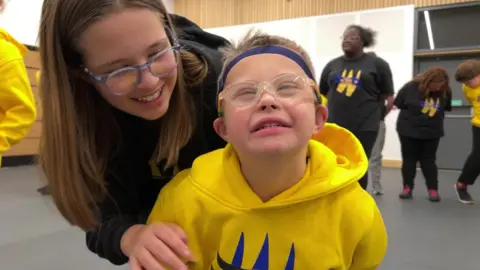 Two children, a girl and a younger boy, smile widely