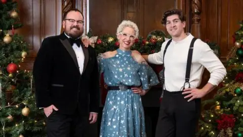 The judges: A man wearing a black velvet suit and bow tie, a woman wearing a blue star print dress and a man in a white shirt with black trousers and suspenders. 