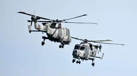 Getty Images Royal Navy Black Cats display team in two Lynx helicopters, which are painted with a camouflage design, the appear to be flying towards one another which is part of the team's aerial display.