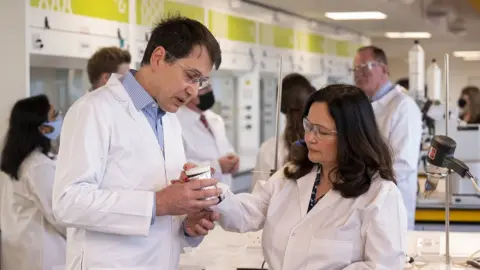 PA Media Natasha's parents examine a beaker while dressed in lab coats and protective glasses in a lab at Southampton University