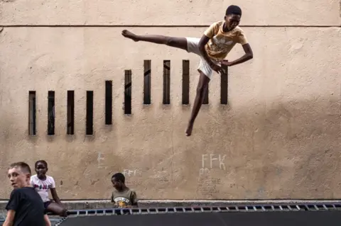 EMMANUEL CROSET/AFP A child jumps on a trampoline as others wait their turn, in Alexandra, near Johannesburg.