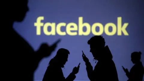 Reuters Silhouettes of mobile users are seen next to a screen projection of Facebook logo in this picture illustration taken March 28, 2018.