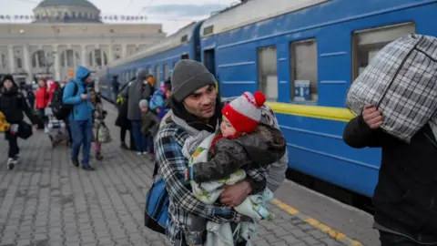 Getty Images A man carries a child as he boards a train at a railway station in Odessa on 9 March 2022.