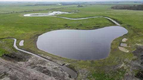 An aerial view of a flat landscape with a large pond in the centre and other rivulets nearby.
