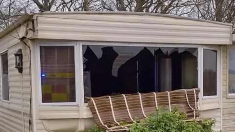 Essex Fire and Rescue Service The outside of a badly damaged caravan. Its front window is smashed.