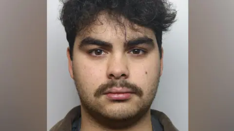 Thames Valley Police Kyran Smith, a man with black curly hair and a dark moustache, is pictured in a police mugshot. 