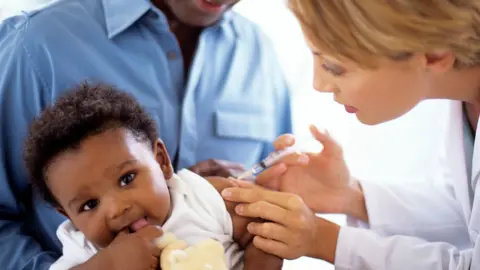 Getty Images A doctor gives a 5-month-old boy an injection, while he sits in his father's lap (stock photo)