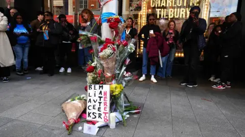 PA Media A flower memorial on a lamppost. A sign that says 'black lives matter here too' is at the front.