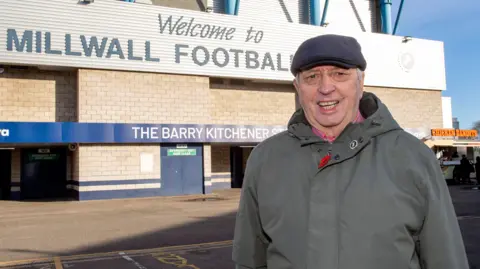 Brian Tonks David Sullivan is wearing a grey jacket and a dark grey cap. He is standing outside Millwall's stadium.