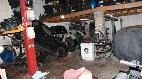 The inside of a garage showing a black cab suspended at its back end on a red metal column, while its front is resting on the ground