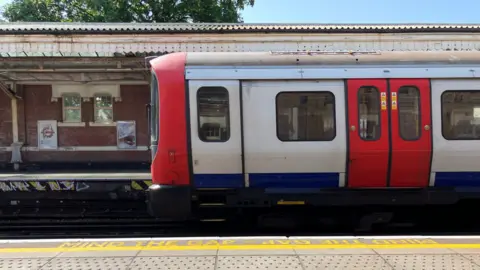 Red and white Tube train pulls into platform side on with a yellow 'mind the gap sign' in foreground